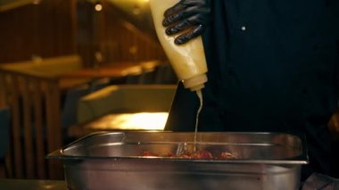 Bir restoranda, merkez salonundaki bir kaburga barında siyah eldivenli şef demir bir kaba çiğ domuz eti serpiyor çeşitli baharatlarla.