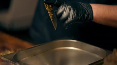 Lokantada yakın plan bir restoranda merkez salondaki bir kaburga barında ahşap bir tahtanın üzerinde siyah eldivenlerle Dijon hardal öğüterek demir bir klozete dökülüyor.