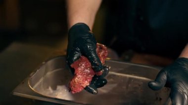 Lokantada yakın plan bir restoranda merkez salonda bir kaburga barda siyah eldivenli bir demir kasede et parçalarıyla terbiye edilmiş salamurayı karıştırıyor.