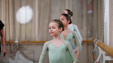 Çocuklar için profesyonel bale okulunu kapatın. Barda antrenörlük eğitimi alan yeşil elbiseli kızlar.