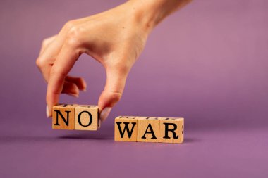 Menekşe sıcacık arka plan, gölgeli kadın eli, siyah harfli ahşap küpler, savaş yok diyor.