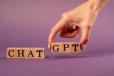 Menekşe, gölgeli sıcak bir arka plan. Kadın eli, siyah harfli ahşap küpler. Kelime dağarcığı, GPT Al.
