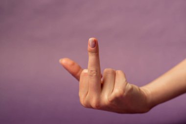 Beautiful female hand on isolated on purple background nude manicure hand shows dissatisfaction gesturing in conflict middle finger fuck