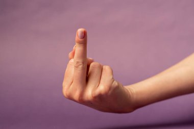 Beautiful female hand on isolated on purple background nude manicure hand shows dissatisfaction gesturing in conflict middle finger fuck