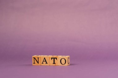 Siyah harfli, gölgeli tahta küplerle mor, ılık bir arka plan ve NATO harflerinden kelimeler.