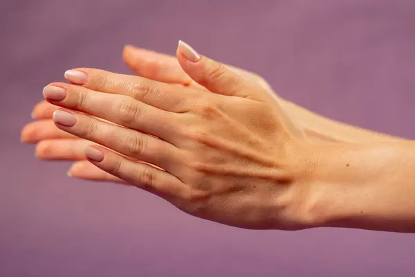 stock image Beautiful female hand on isolated on purple background sign language applause hand hitting another nude manicure