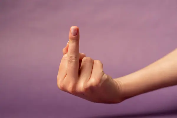 stock image Beautiful female hand on isolated on purple background nude manicure hand shows dissatisfaction gesturing in conflict middle finger fuck