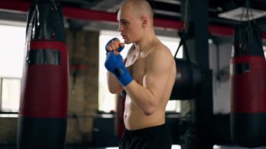 Bir boks kulübüne yakın plan mavi bandajlı kel genç bir boksör gölge boksu profesyonel tekniğini yumrukluyor.