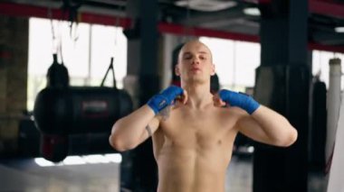 Bir boks kulübüne yakın plan mavi bandajlı kel genç bir boksör gölge boksu profesyonel tekniğini yumrukluyor.