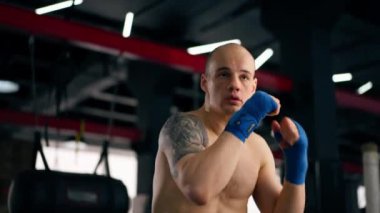 Bir boks kulübüne yakın plan mavi bandajlı kel genç bir boksör gölge boksu profesyonel tekniğini yumrukluyor.