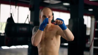 Bir boks kulübüne yakın plan mavi bandajlı kel genç bir boksör gölge boksu profesyonel tekniğini yumrukluyor.