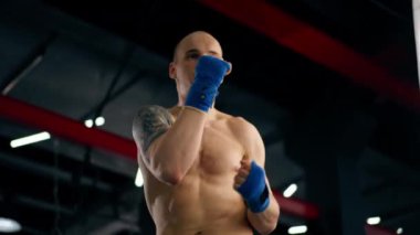 Bir boks kulübüne yakın plan mavi bandajlı kel genç bir boksör gölge boksu profesyonel tekniğini yumrukluyor.