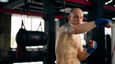 Bir boks kulübüne yakın plan mavi bandajlı kel genç bir boksör gölge boksu profesyonel tekniğini yumrukluyor.