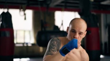 Bir boks kulübüne yakın plan mavi bandajlı kel genç bir boksör gölge boksu profesyonel tekniğini yumrukluyor.