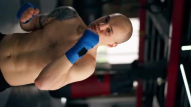 Bir boks kulübünde düşey video. Mavi bandajlı kel bir boksör. Trenler gölge boksu profesyonel tekniğini yumrukluyor.