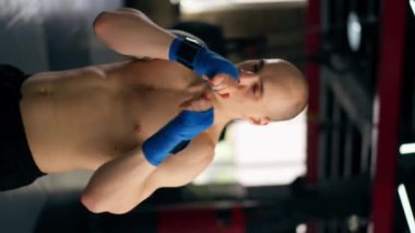 Bir boks kulübünde düşey video. Mavi bandajlı kel bir boksör. Trenler gölge boksu profesyonel tekniğini yumrukluyor.