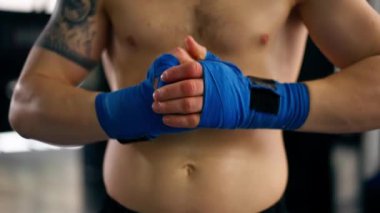 Bir boks dövüş kulübünde mavi bandajlı kel ve genç bir boksör profesyonel bir antrenmandan önce ellerini uzatıyor.