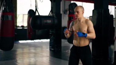 Bir boks dövüş kulübünde kel, mavi bandajlı genç bir boksör profesyonel dövüş tekniğinden önce bir tekme eğitiyor.