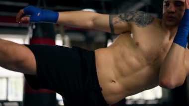 Bir boks dövüş kulübünde kel, mavi bandajlı genç bir boksör profesyonel dövüş tekniğinden önce bir tekme eğitiyor.