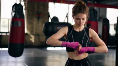 Bir boks kulübünde siyah kazaklı genç bir kız ellerini boks antrenmanına hazırlamak için pembe elastik bandajlar sarar.