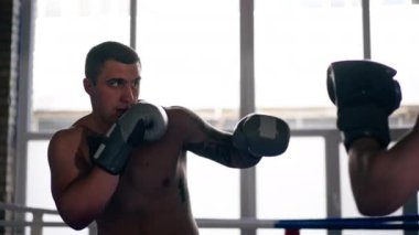 Bir boks kulübünde. İki çıplak göğüslü boksör. Gri eldivenli dövmeli.