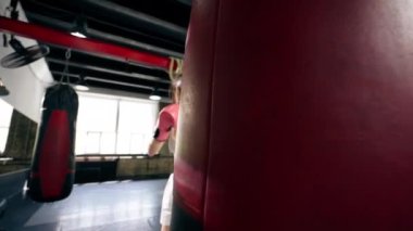 Dövüş kulübünde pembe eldivenli beyaz üniformalı genç bir kız kırmızı bir çanta üzerinde teknik tekme ve yumruk pratiği yapıyor.