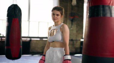 Boks kulübünde beyaz profesyonel üniformalı genç bir kız. Pembe eldivenli. Verimli bir gün geçirdikten sonra yoruldu.