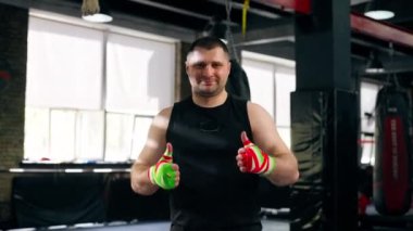 Bir boks kulübünde siyah tişörtlü yaşlı bir kas çalıştırıcı ve çok renkli bandajlarla iyi bir egzersizden sonra mutlu olur.