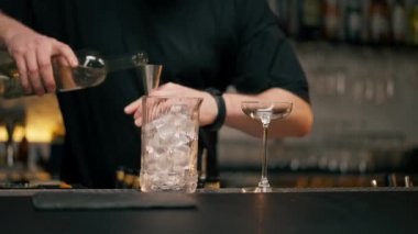 Barmen, barmene içki doldururken barmen ölçü kabına alkol dolduruyor.