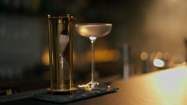 Tezgahın üzerinde serinletici bir bardak var yanında da martini ve altın bir kum saati.