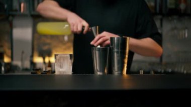 Erkek barmen elleri şişeyi tutuyor ve içeceği ustalıkla çelik jigger 'a dolduruyor.