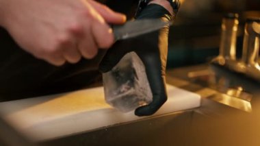 Siyah tişörtlü, buzu keskin bir bıçakla kesen erkek barmenin yakın çekimi.