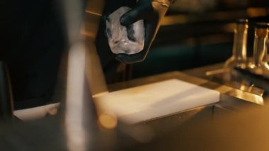 Siyah tişörtlü, buzu keskin bir bıçakla kesen erkek barmenin yakın çekimi.