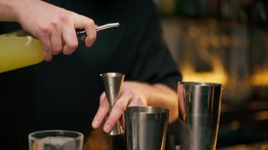 Yakın plan erkek barmen elleri şişeyi tutuyor ve içkiyi ustaca jigger 'a döküyor.