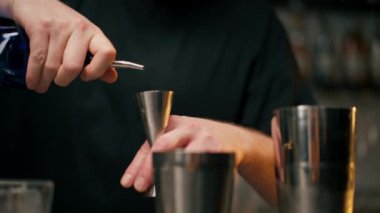 Yakın plan erkek barmen elleri şişeyi tutuyor ve içkiyi ustaca jigger 'a döküyor.