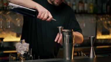 Yakın plan erkek barmen elleri şişeyi tutuyor ve içkiyi ustaca jigger 'a döküyor.