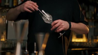 Profesyonel bir barmen, bulanık bir arkaplanda güzel bir bardakta buz gibi bir kokteyl karıştırır.