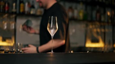 Önlüklü genç bir barmen içki hazırlıyor. Barın önünde kokteyl bardağıyla sallıyor.