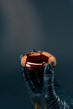 Siyah ve mavi arka planda bir kadın, siyah eldivenli bir kadın elinde çikolatalı karamelli kurabiyelerle kurabiyelerin üzerine dökülüyor.
