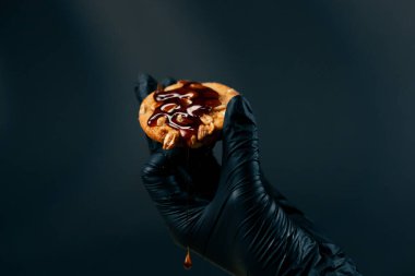 Siyah ve mavi arka planda bir kadın, siyah eldivenli bir kadın elinde çikolatalı karamelli kurabiyelerle kurabiyelerin üzerine dökülüyor.