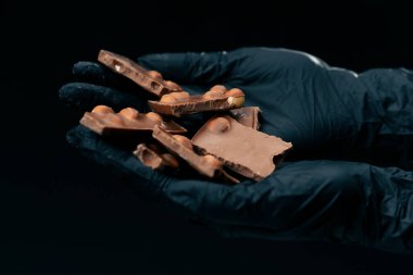 Siyah ve mavi bir arkaplanda düz beyaz bir plaka, siyah eldivenli kadın elleri fındıklı çikolata tutuyor.