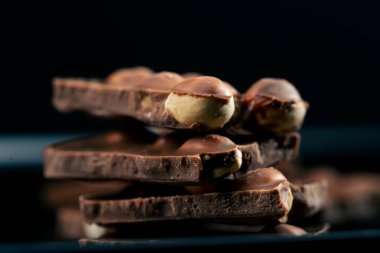 Siyah bir tabaktaki siyah mavi arka planda fındıklı sütlü çikolata parçalanmış.