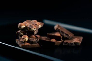 Siyah bir tabaktaki siyah mavi arka planda fındıklı sütlü çikolata parçalanmış.