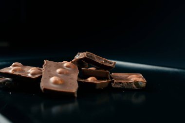 Siyah bir tabaktaki siyah mavi arka planda fındıklı sütlü çikolata parçalanmış.