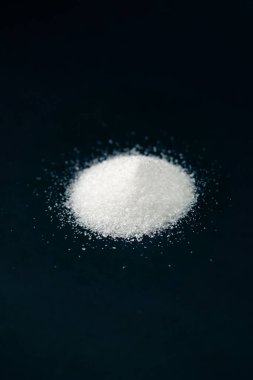 Siyah-mavi arka planda yakın plan beyaz granüle şeker uzanıyor, şeker yığınının etrafındaki kristal topaklar sağlığa zararlıdır