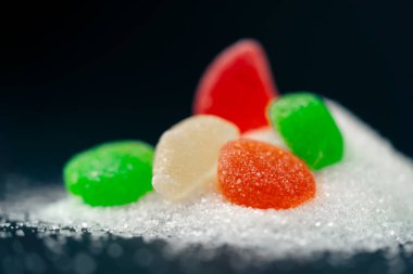 Koyu mavi arka planda, yan ışıklandırması olan, şeker serpiştirilmiş çok renkli jöleler sağlığa zararlı bir şeker kaydırağının üzerine serpiştirilir.