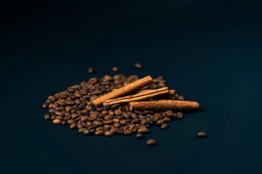 Siyah ve mavi arka planda kavrulmuş kahve çekirdeklerine yakın plan. Arka planda birkaç tarçın çubuğu ve baharatlı kahve tarifi var.