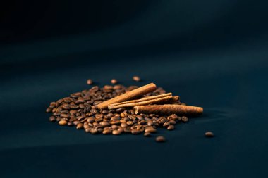 Siyah ve mavi arka planda kavrulmuş kahve çekirdeklerine yakın plan. Arka planda birkaç tarçın çubuğu ve baharatlı kahve tarifi var.