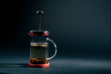 Koyu mavi arka planda, yan ışıklandırmayla birlikte yeşil çay demleyen modern bir çaydanlık var.