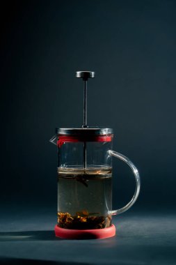 Koyu mavi arka planda, yan ışıklandırmayla birlikte yeşil çay demleyen modern bir çaydanlık var.